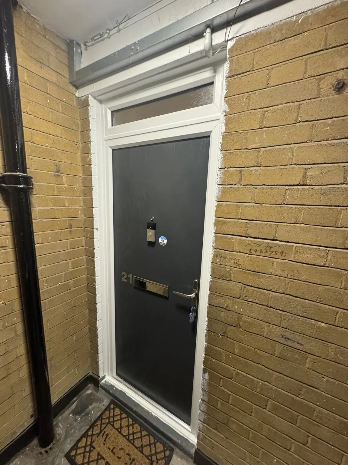 Dark residential entrance door installed within a white frame against external brickwork