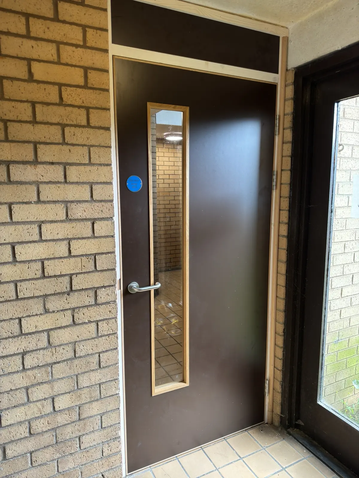 Dark glazed corridor door installed in a brick communal entrance