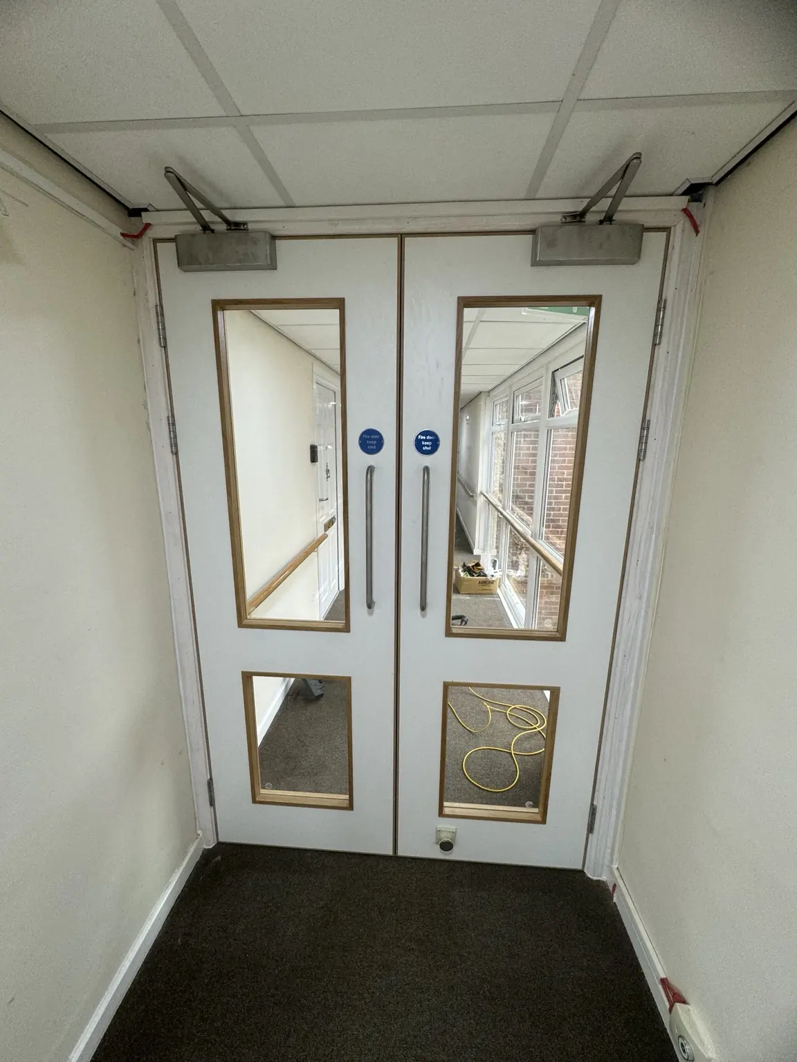 White glazed double doors with overhead closers in a communal corridor