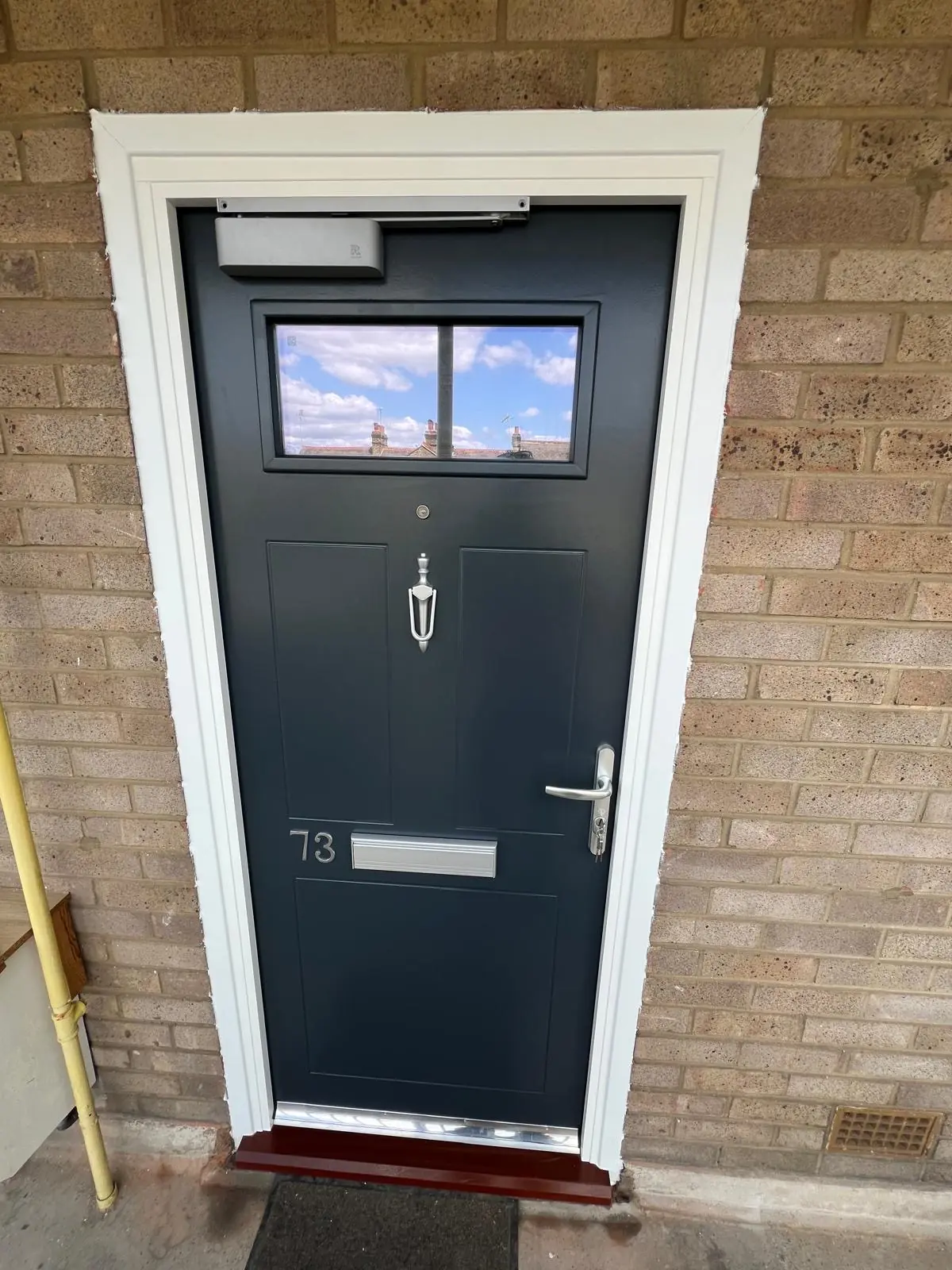 Dark residential entrance door with a wide upper glazed panel and overhead closer