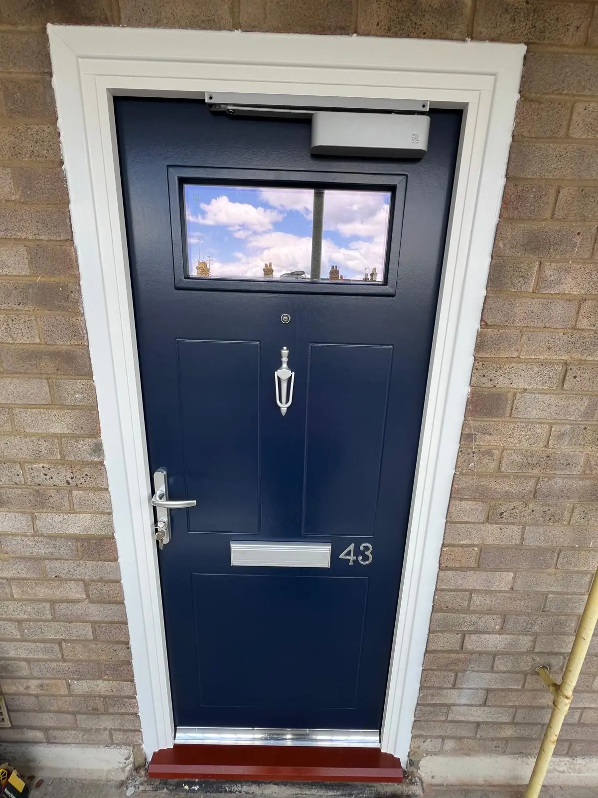 Dark residential entrance door with glazed upper panel in an external brick opening