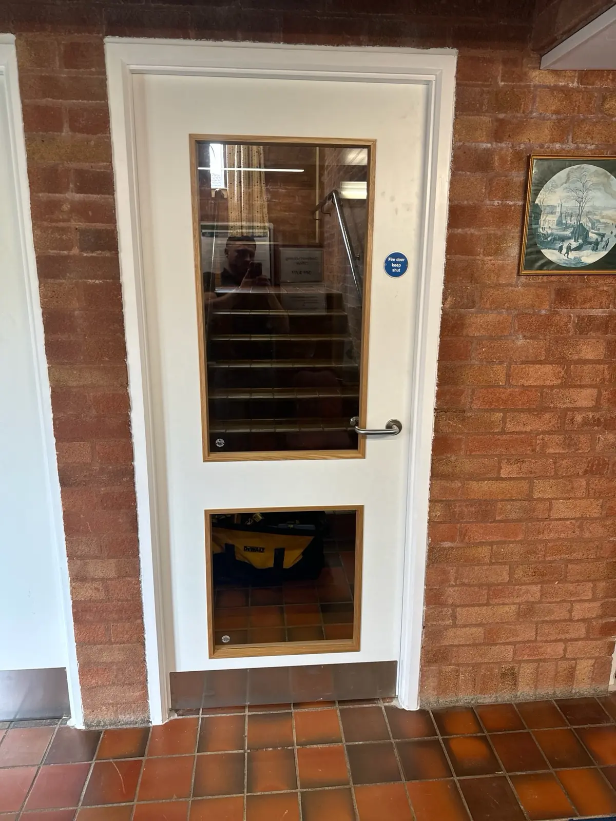 White communal door with two glazed vision panels in a brick-walled corridor
