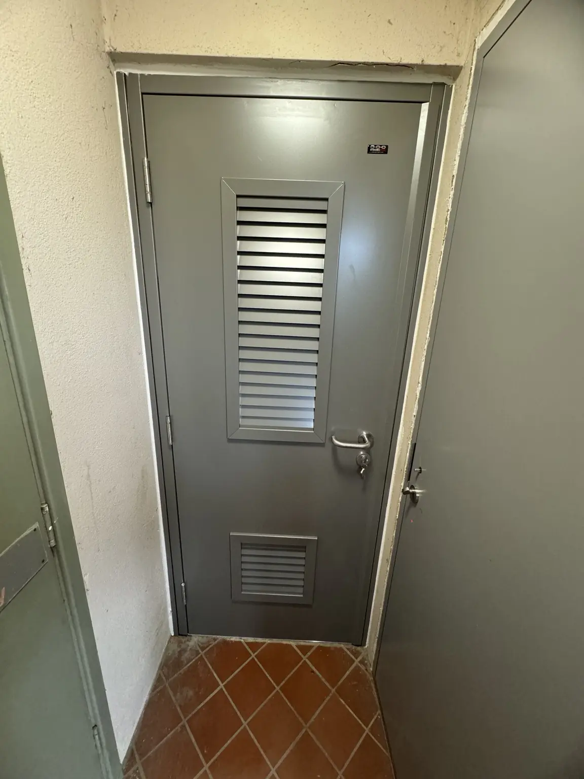 Grey metal service door with upper and lower ventilation louvres