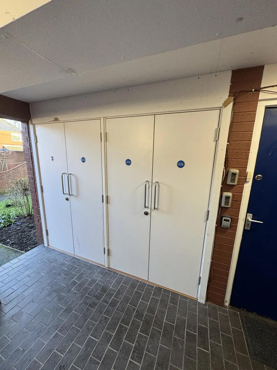 White multi-leaf communal and service door bank beneath a sheltered walkway