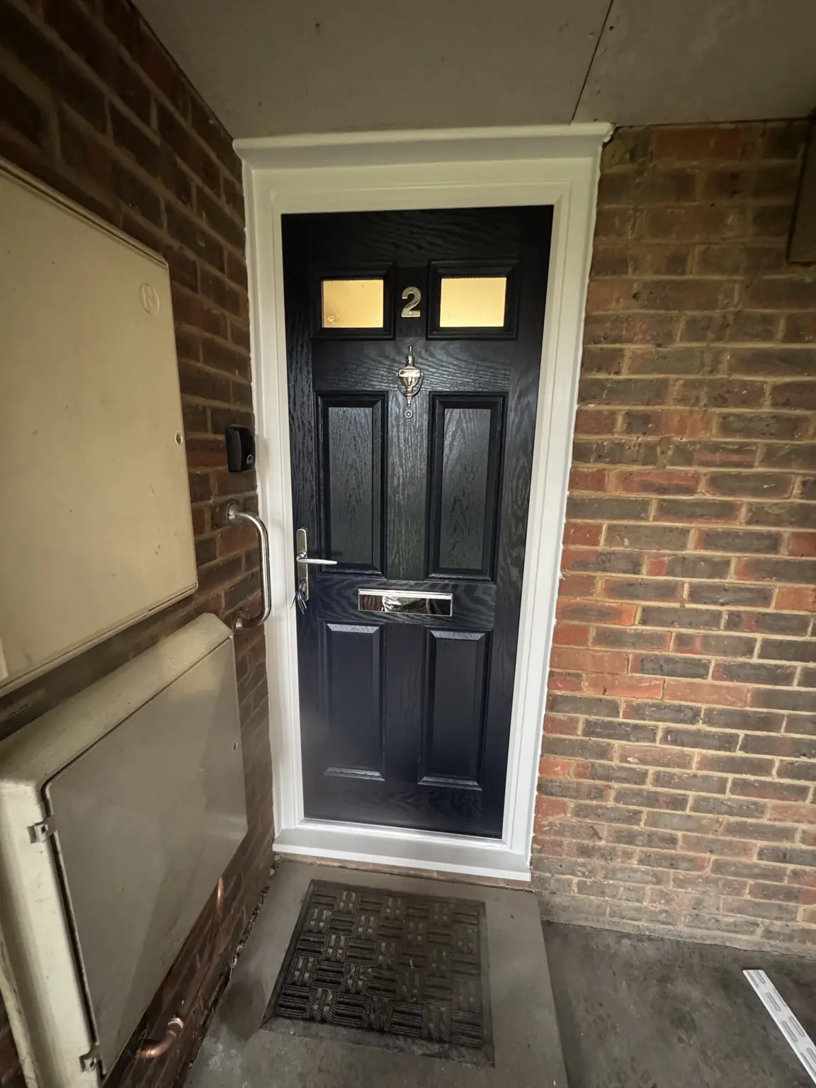 Dark panelled flat-entrance door with letter plate, viewer and lever handle