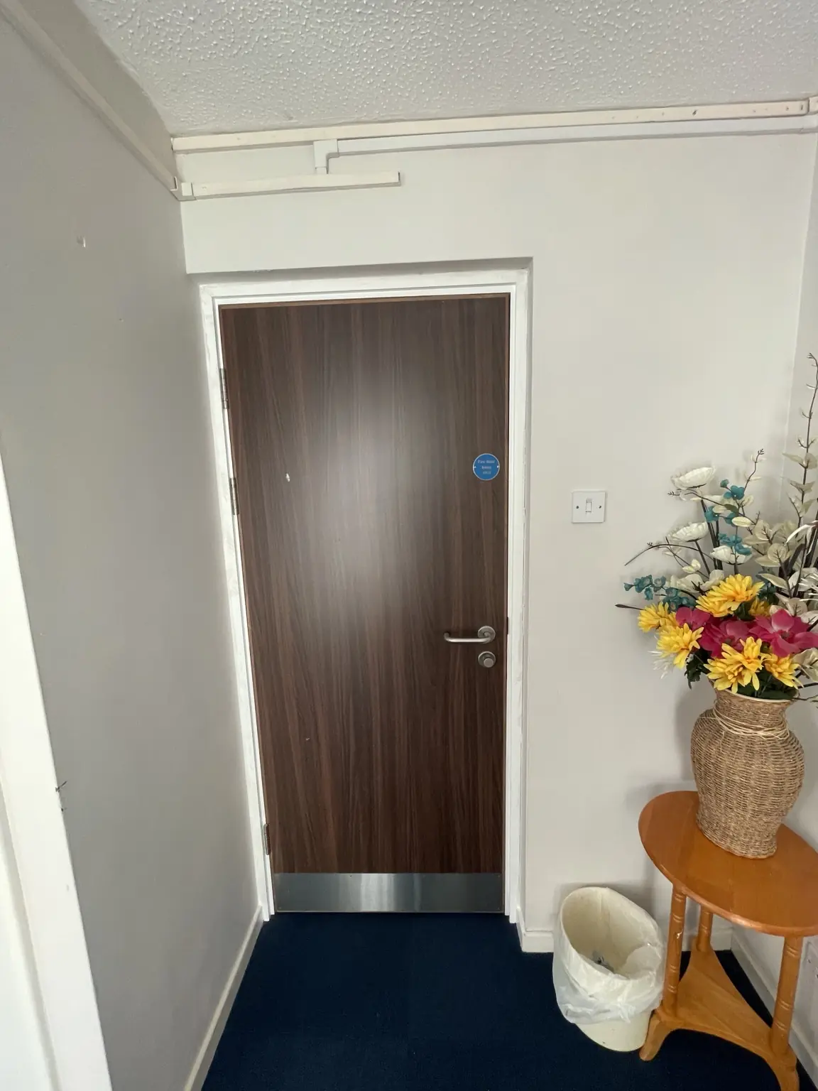 Completed timber communal doorset with threshold strip and fire-door signage