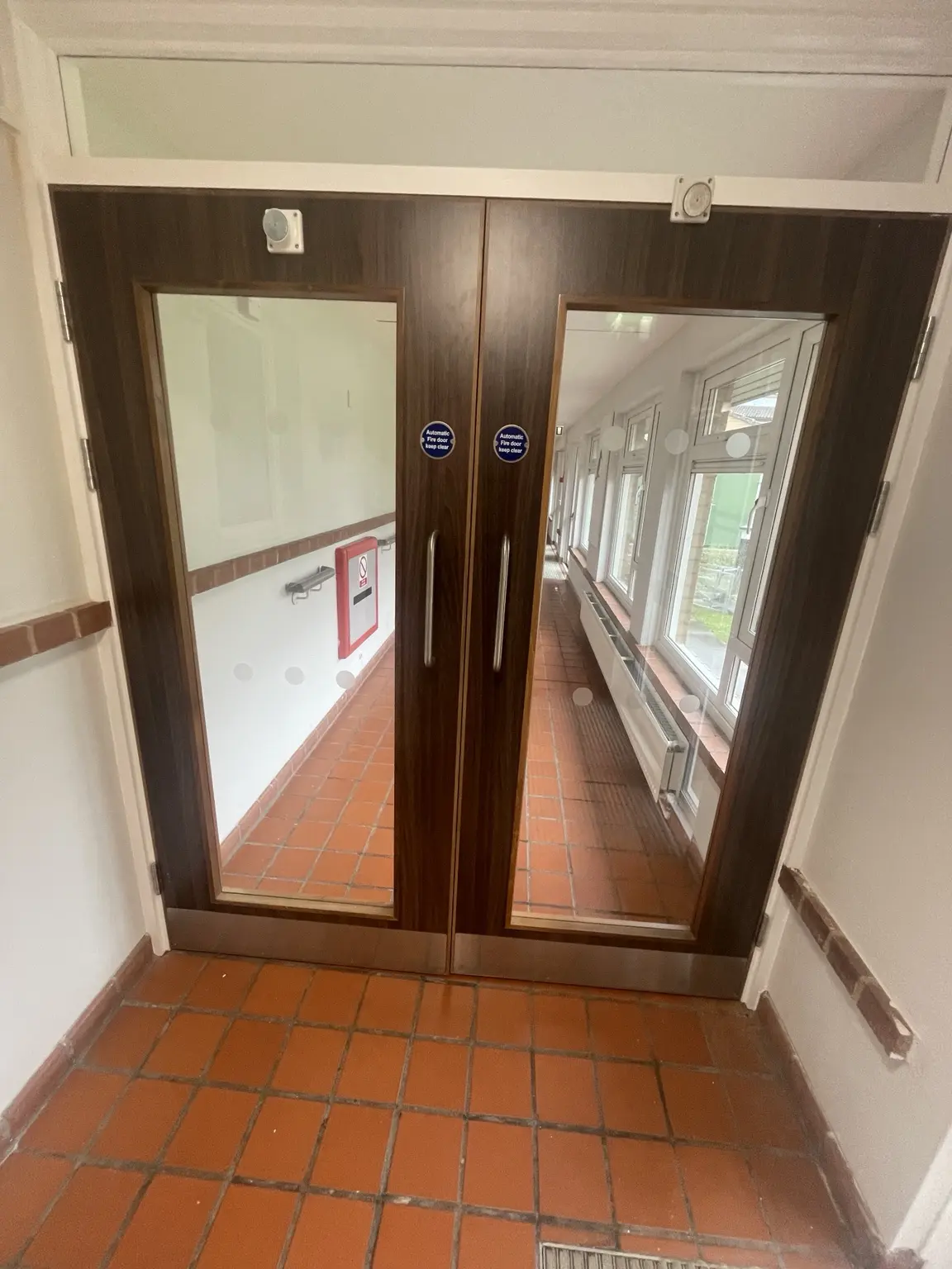 Timber-effect glazed double doors in a bright communal corridor